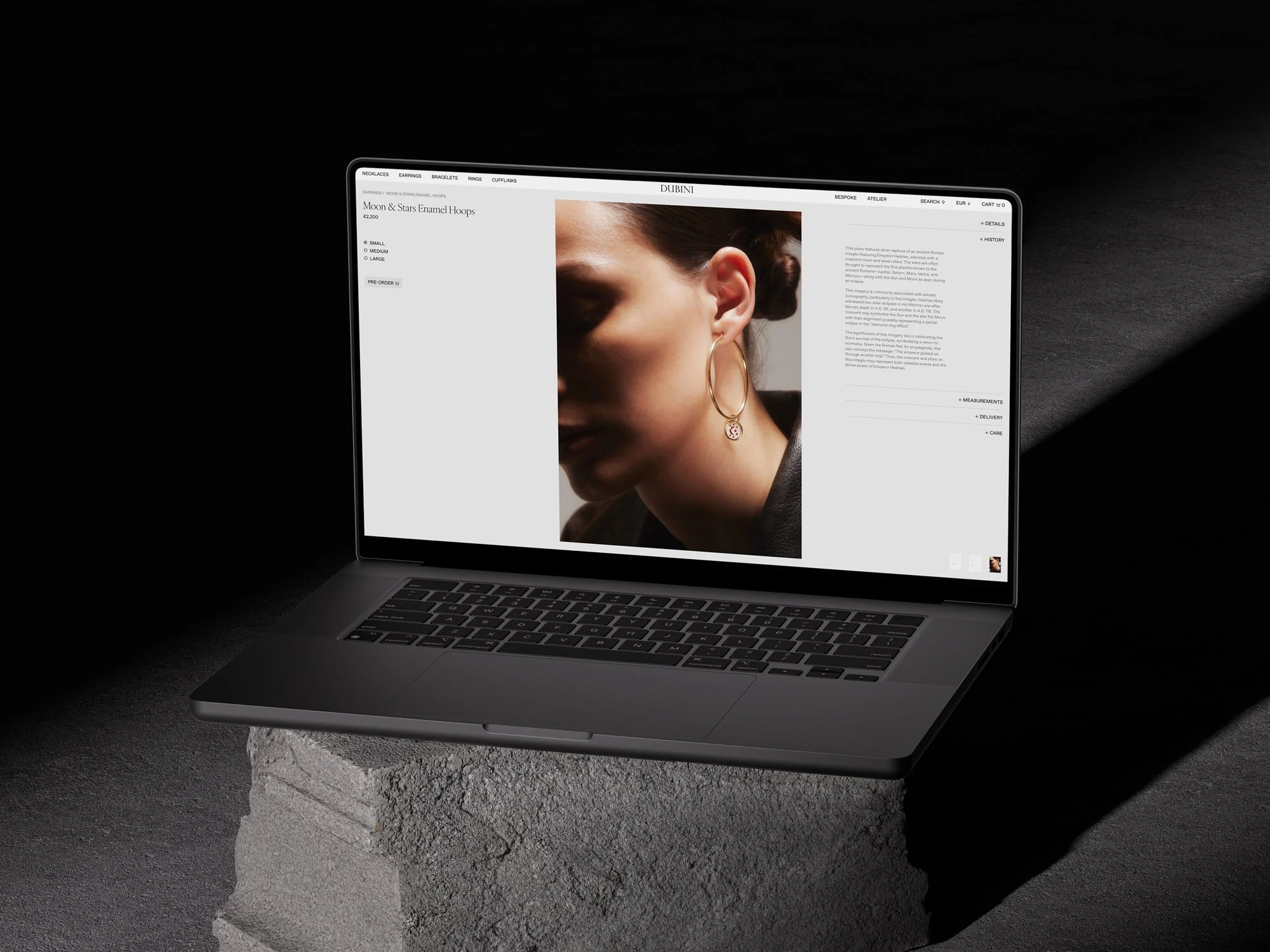 Laptop on a concrete block showing a product page with a model wearing gold Moon & Stars hoop earrings, for Dubini.