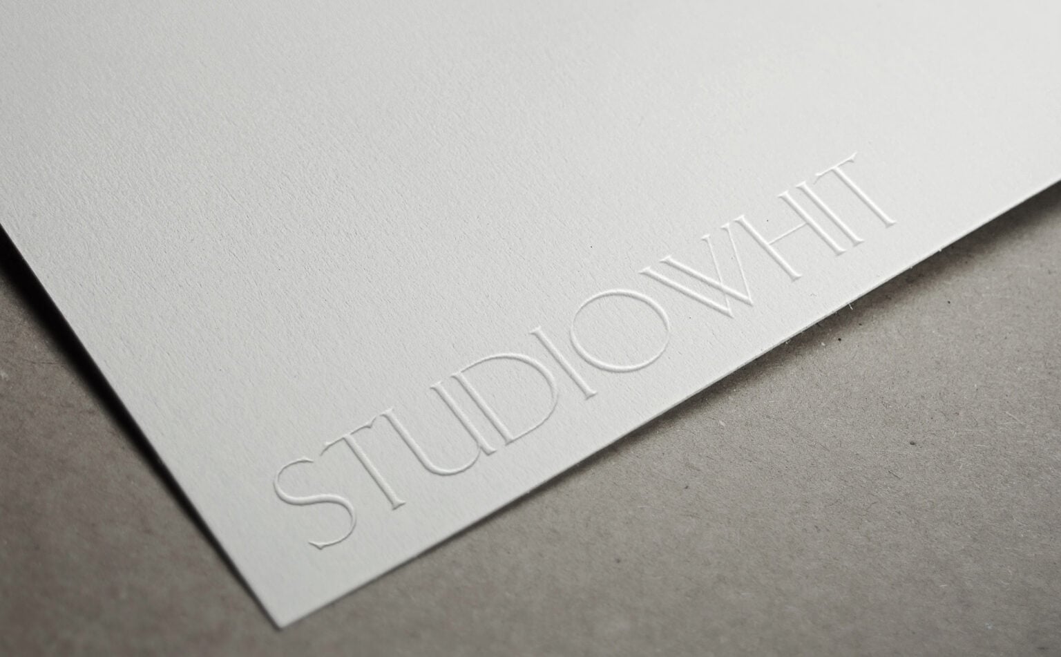 Wordmark blind embossed on textured white paper resting on a grey surface, for Studio Whit.