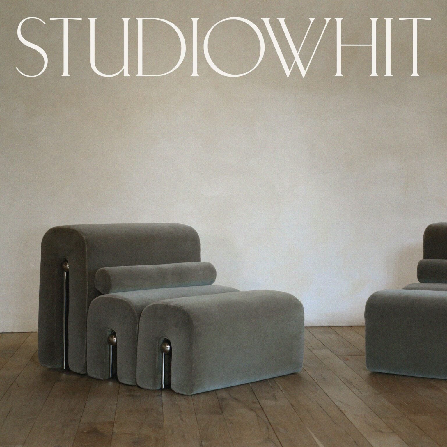 Grey velvet modular lounge chair with chrome legs on a wooden floor, under a white wordmark, for Studio Whit.