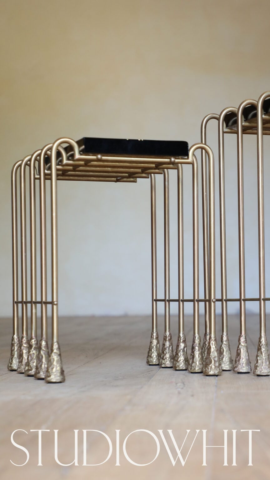 Brass nesting side tables with black tops and textured feet on a wooden floor, with the wordmark below, for Studio Whit.